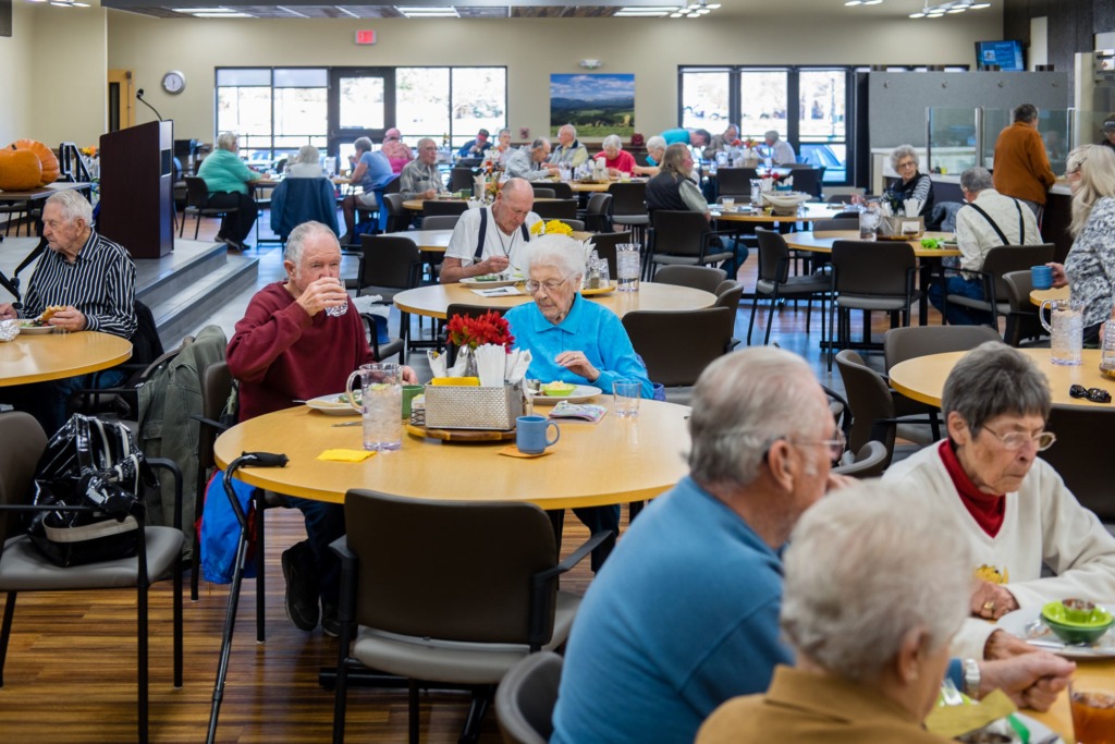 Image of our patrons sitting around numerous round tables eating and enjoying eachother's company in our cafe at the Hub.